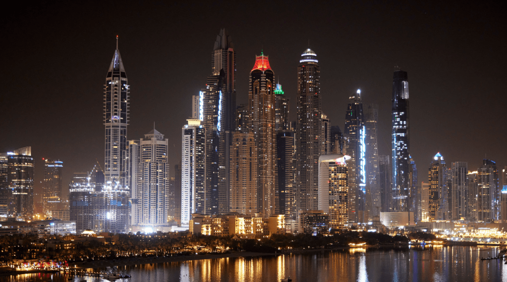 A nighttime cityscape of Dubai with illuminated skyscrapers reflecting on the water, perfect for hosting an unforgettable incentive event Dubai, showcasing the modern skyline against a dark sky.
