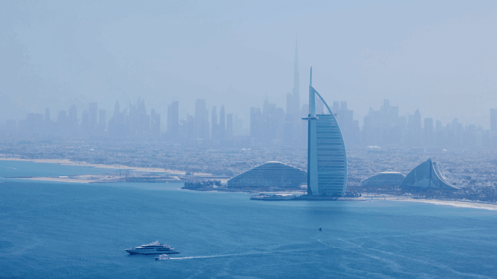A yacht sails on turquoise water near the Burj Al Arab hotel, with Dubai’s hazy skyline—including the Burj Khalifa—framing a perfect scene for an unforgettable incentive event Dubai style.