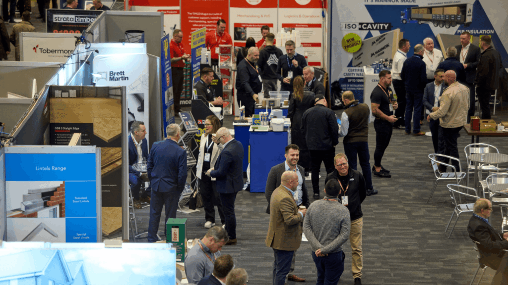 Attendees networking and visiting booths at a busy indoor conference & exhibition, featuring displays, banners, and informational stands focused on the building and construction industries.
