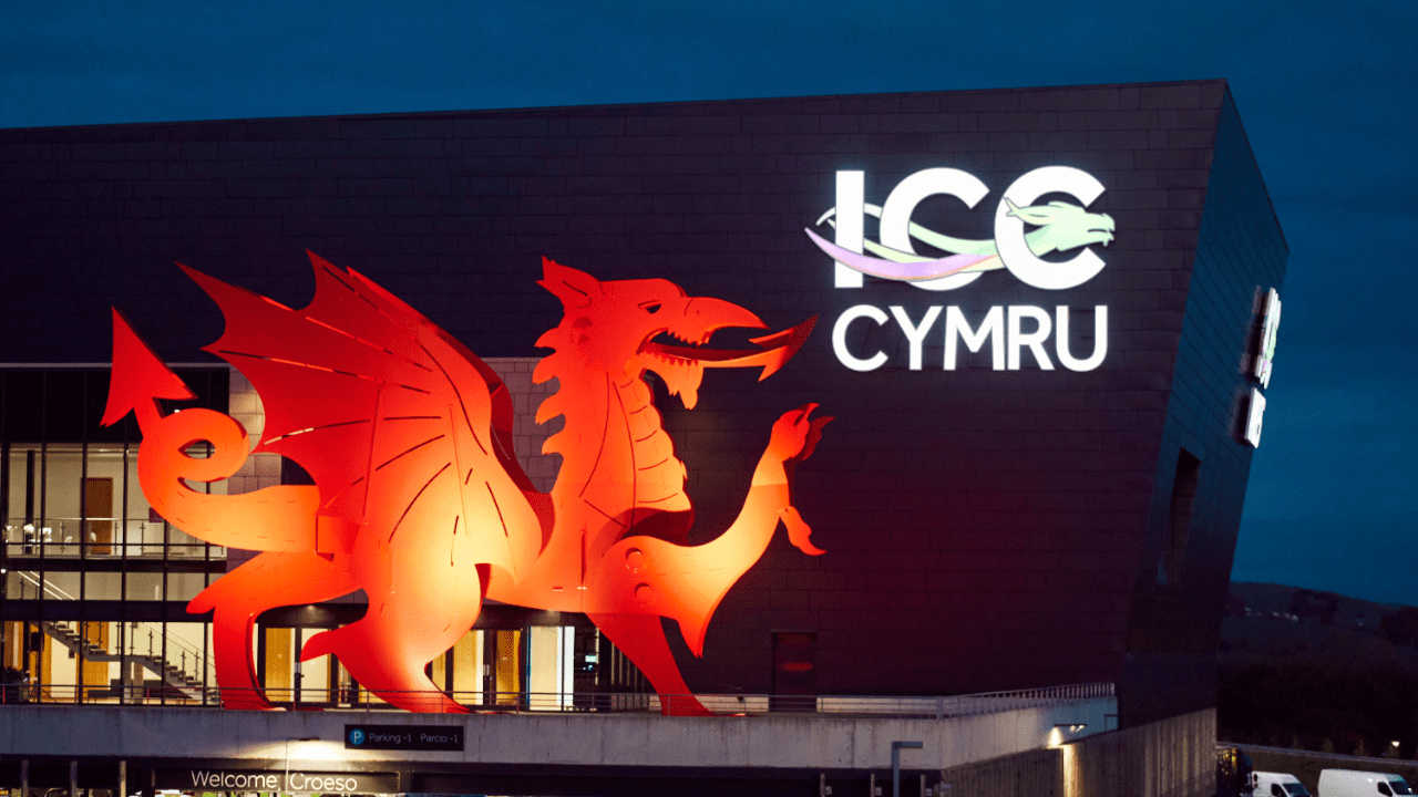 A large red Welsh dragon is illuminated on the exterior of the ICC Cymru building at dusk, with the venue’s logo and name in white and purple lights nearby—an impressive sight for any event space finder seeking a unique location.
