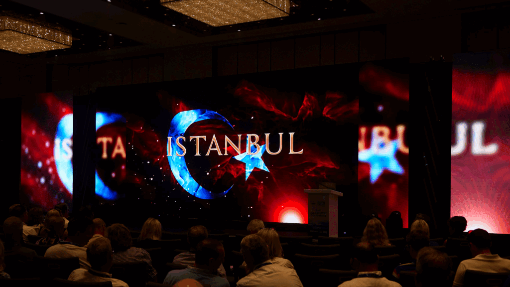 A large audience faces a stage with a bright screen displaying a crescent moon and star alongside “ISTANBUL” in bold letters, suggesting a sustainable conference or event centered on the city.