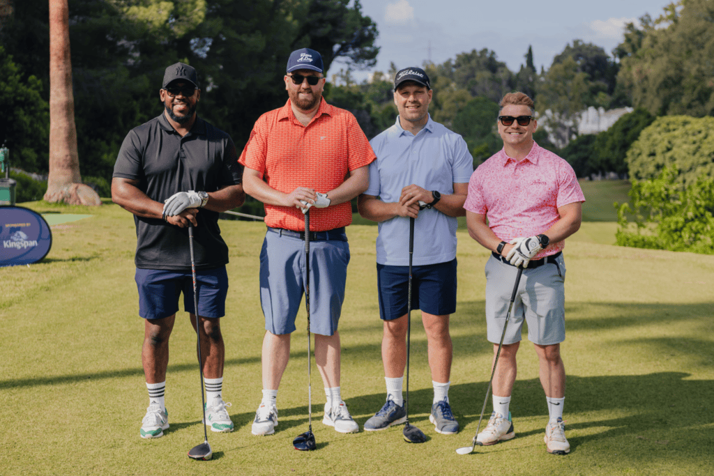 Four men stand on a golf course, smiling at the camera with golf clubs in hand. Dressed in classic golf attire—including hats and sunglasses—they are enjoying a day out as part of an incentive travel programme. Surrounded by lush green grass and trees under a sunny sky, the group captures the spirit of camaraderie and reward.