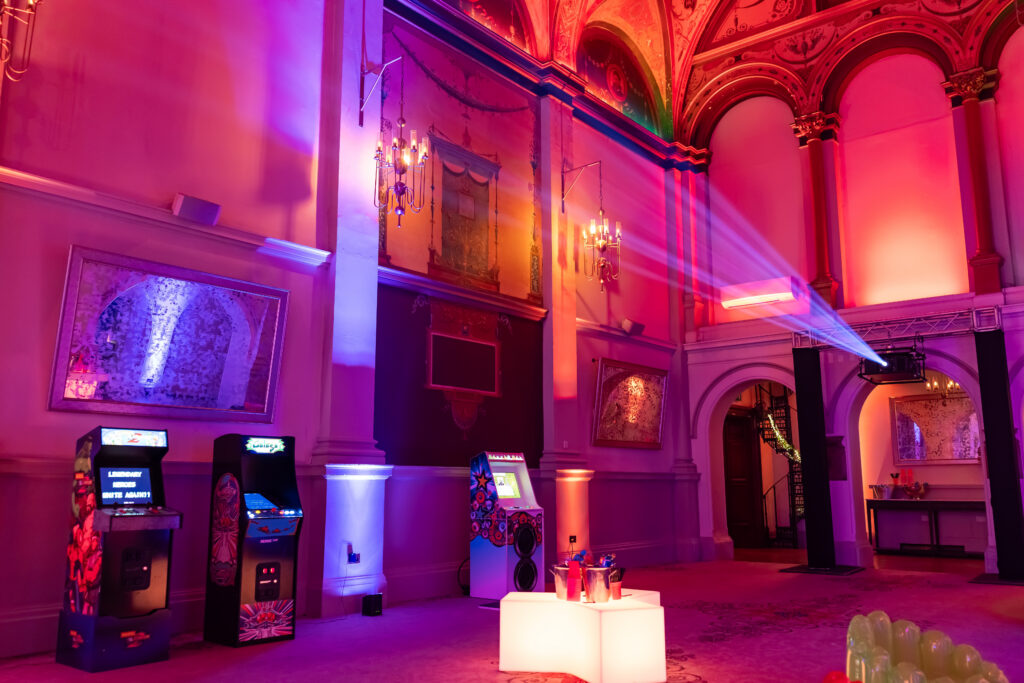 An event space for an advisory board event featuring classic arcade games, a glowing illuminated table, and purple and red lighting.