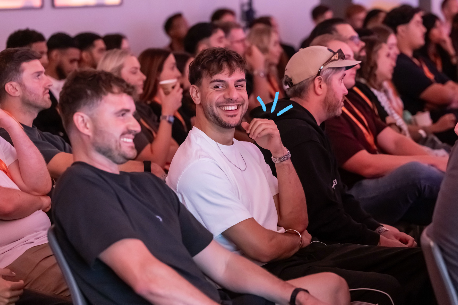 A smiling young man in a white T-shirt sits among an audience at an event, with blue graphic lines radiating from his shoulder to illustrate event marketing effectiveness.
